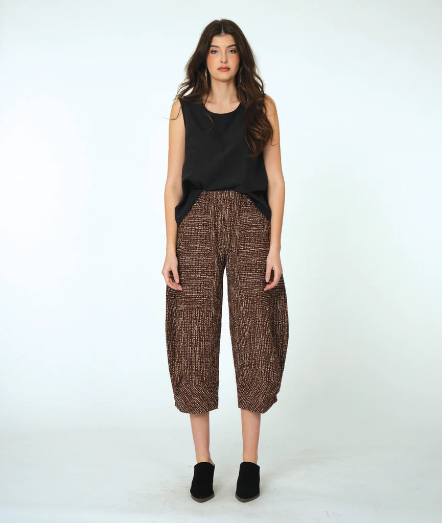 Woman wearing a black sleeveless top and brown patterned pants on a white background
