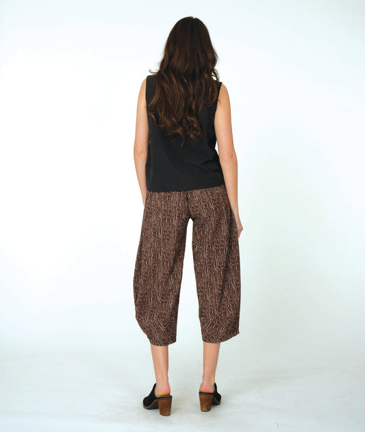 Woman wearing a black sleeveless top and brown patterned pants on a white background