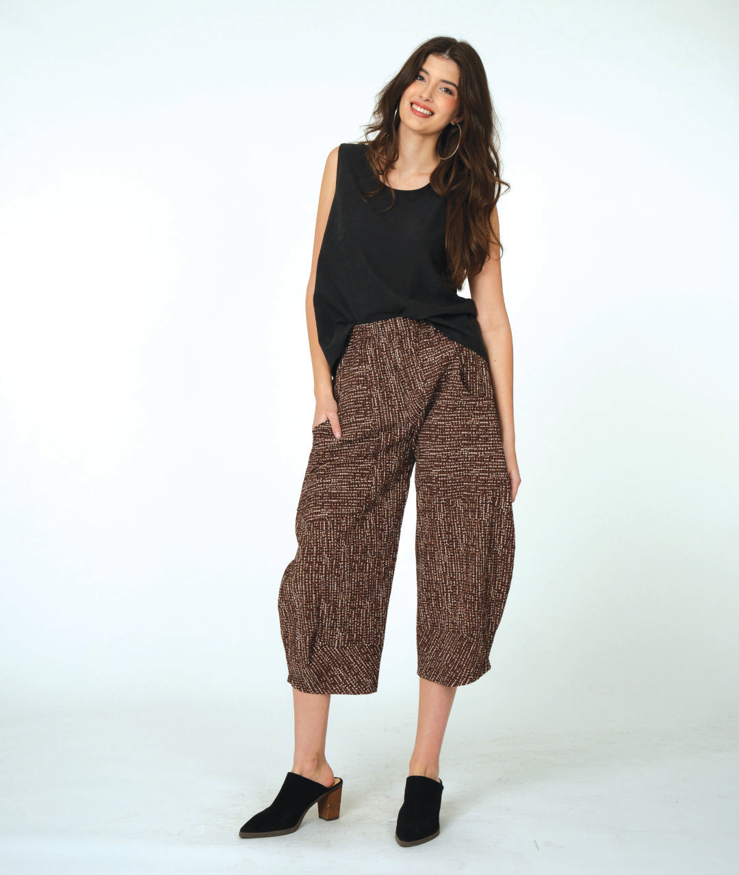 Woman wearing a black sleeveless top and brown patterned pants on a white background