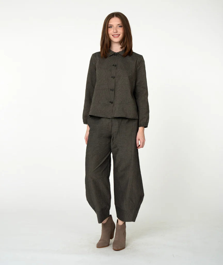 A woman modeling a dark olive green two-piece linen set consisting of a button-front top and matching wide-leg trousers, paired with brown ankle boots, against a plain white studio background.