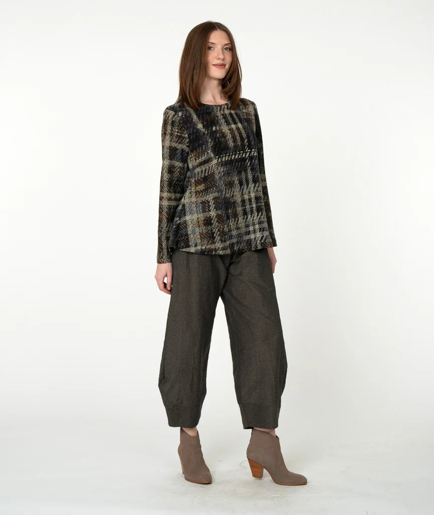 A woman modeling a long-sleeve plaid top in black, beige, and brown tones, paired with dark olive green wide-leg cropped pants and taupe heeled ankle boots, against a plain white studio background.