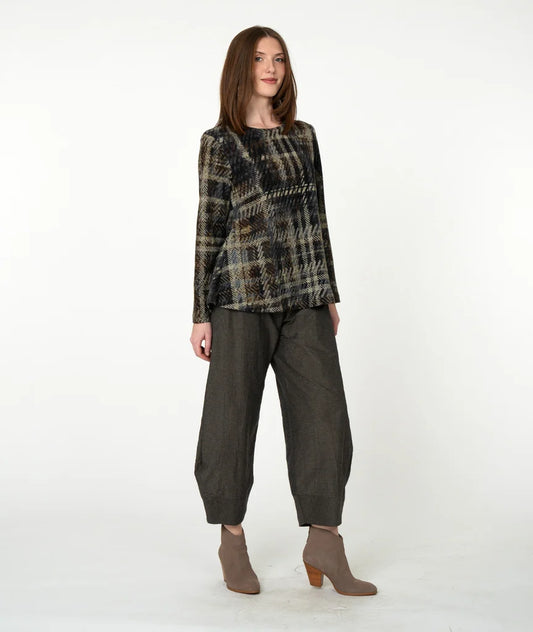A woman modeling a long-sleeve plaid top in black, beige, and brown tones, paired with dark olive green wide-leg cropped pants and taupe heeled ankle boots, against a plain white studio background.
