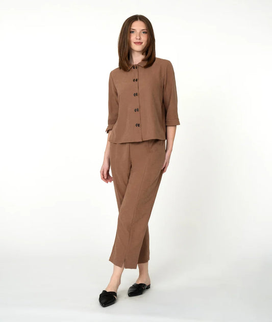 A woman modeling a matching brown two-piece set consisting of a button-front blouse with three-quarter sleeves and straight-leg cropped pants, paired with black flats, against a plain white studio background.