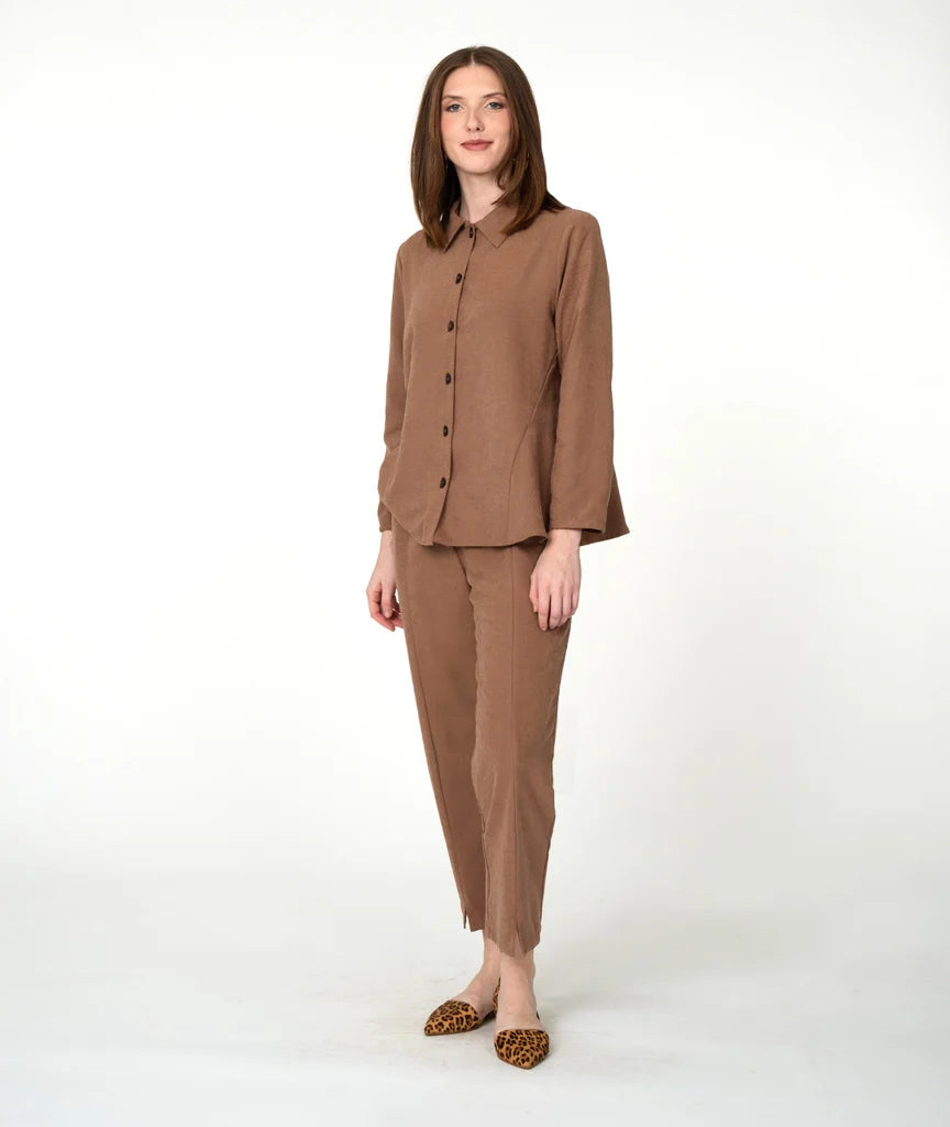 Woman wearing a light brown button up long sleeve top and slim light brown pants on a white background