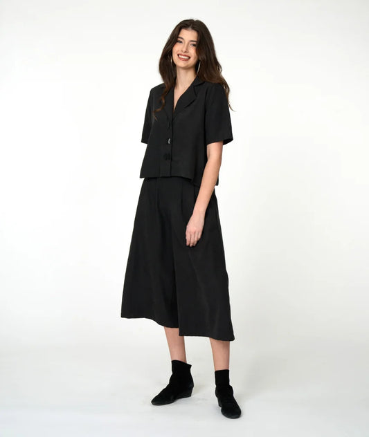 model wearing black button up short sleeve cropped shirt with wide black pants and black shoes