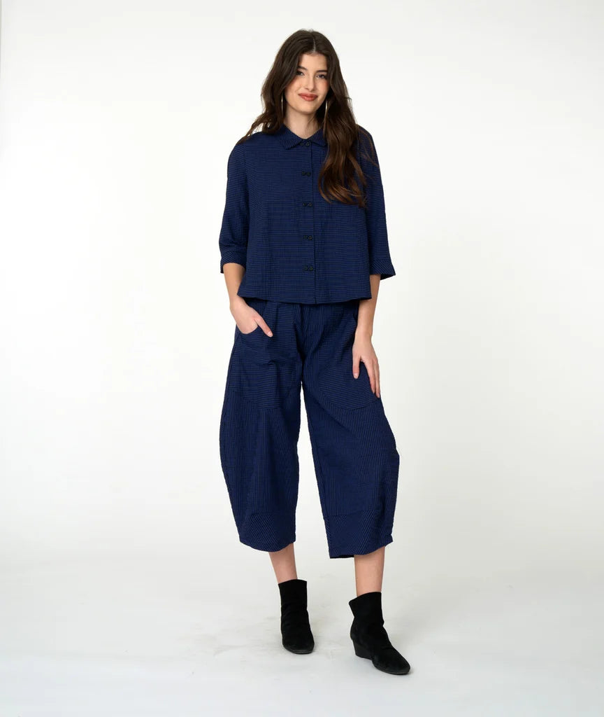 A woman modeling a matching navy blue two-piece outfit consisting of a button-front top with three-quarter sleeves and relaxed wide-leg cropped pants, paired with black ankle boots, against a plain white studio background.