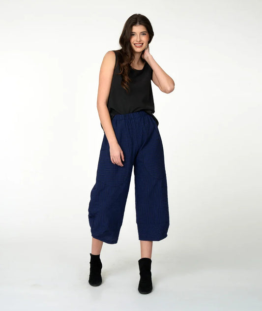 Woman wearing a black sleeveless top and blue wide-leg pants on a white background
