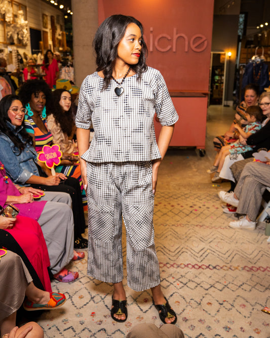 Woman in a checkered outfit and black heart necklace walking down a runway