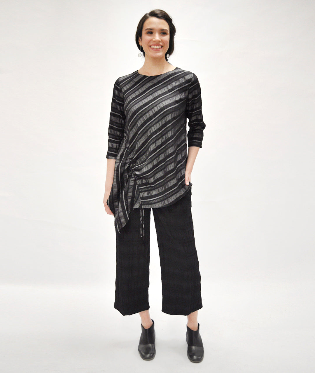 model in a textured black wide leg pant with an asymmetrical grey and black striped top