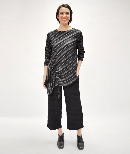 model in a textured black wide leg pant with an asymmetrical grey and black striped top