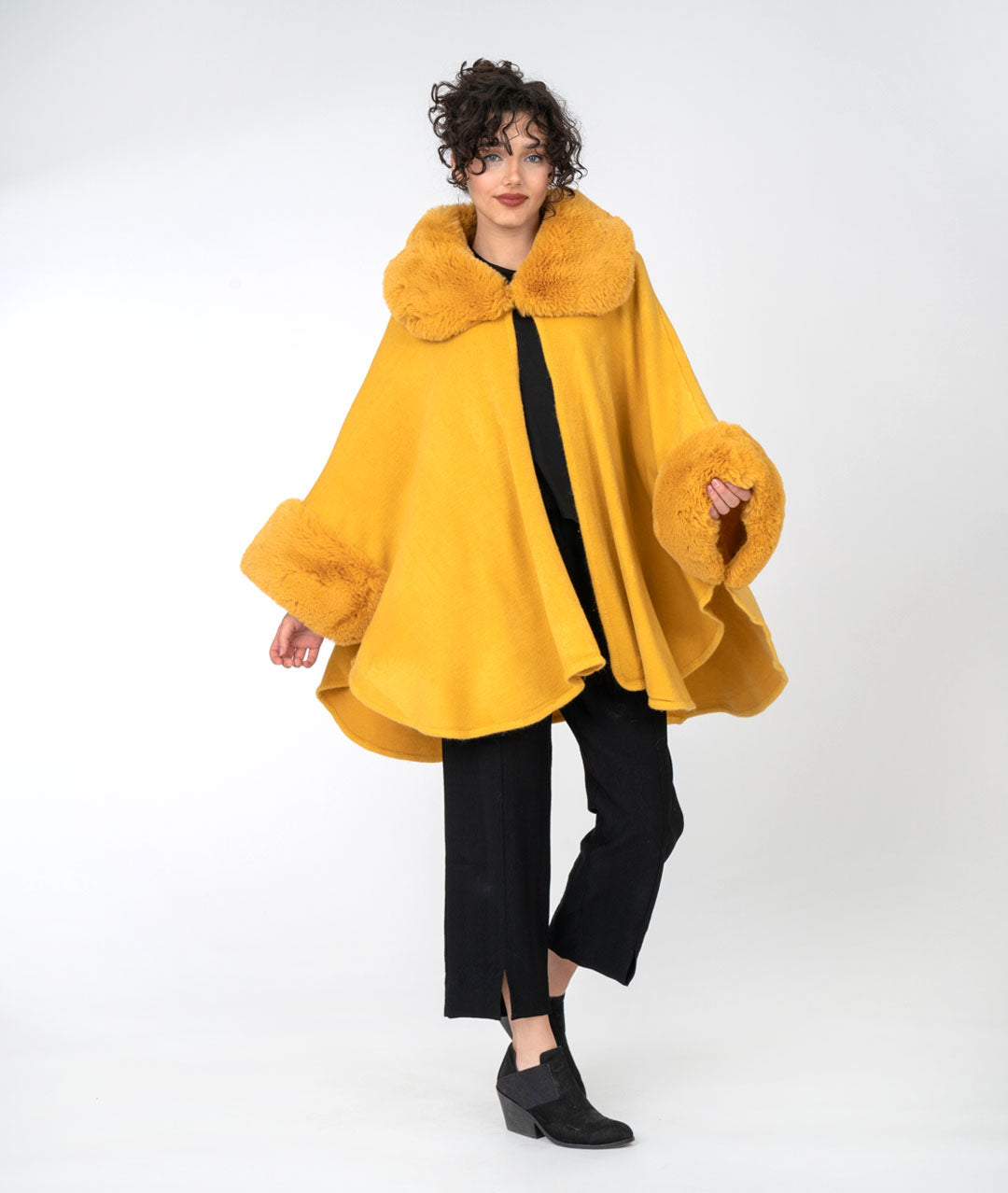 model in an all black outfit with a vibrant gold cape with faux fur sleeves and collar, buttoned at the neck