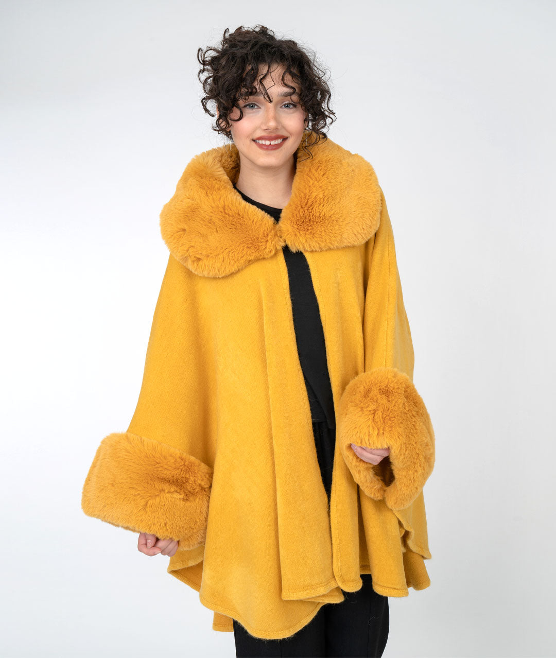 model in an all black outfit with a vibrant gold cape with faux fur sleeves and collar, buttoned at the neck