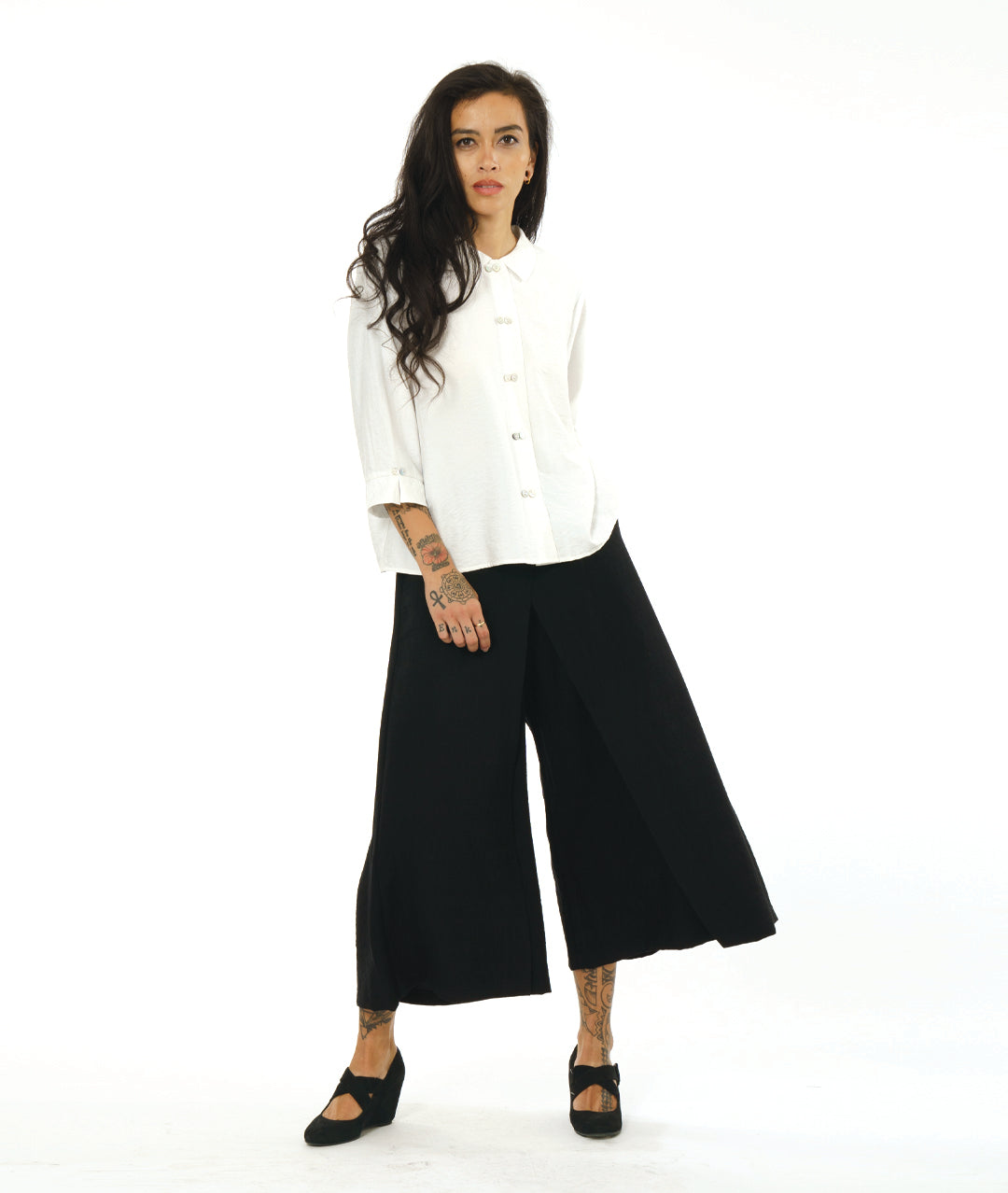 model in a black wide leg pant with overlapping apron panels in the front, worn with a white button down blouse with a twin button detail and 3/4 sleeves