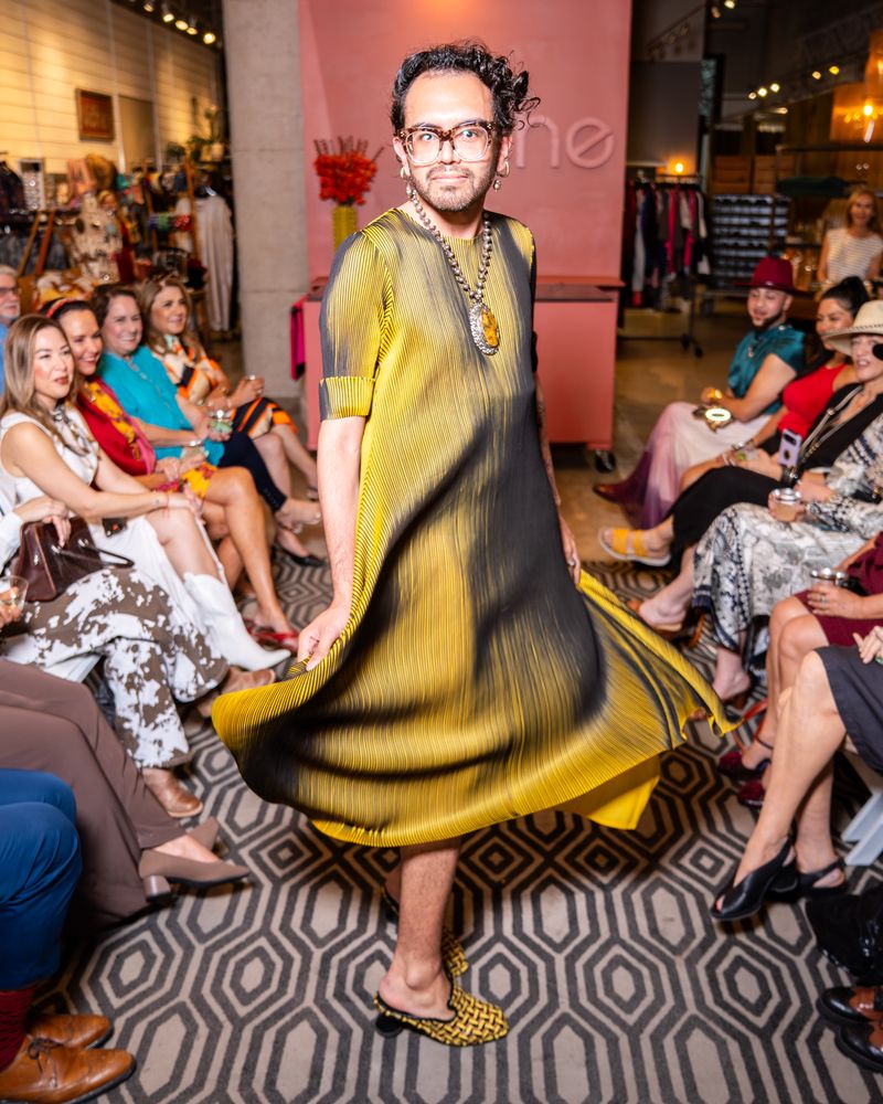 Model in a yellow and black pleated dress walking down a runway