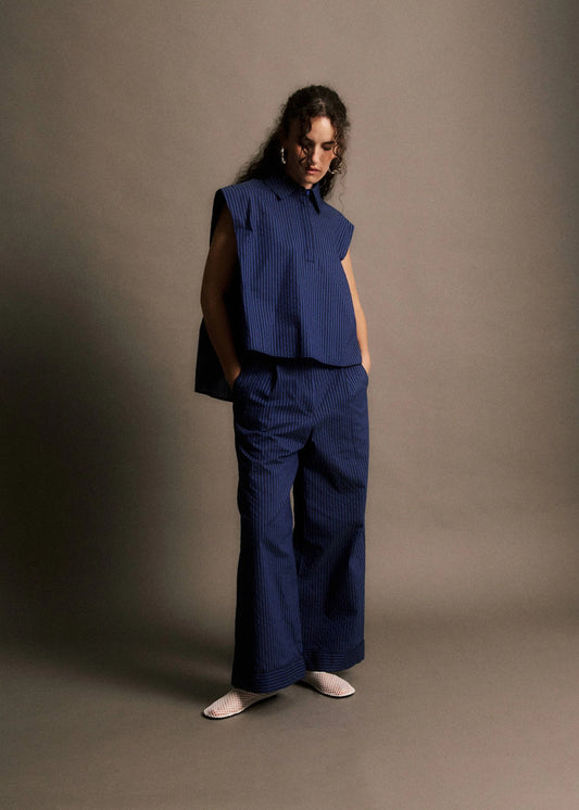 Woman wearing a blue sleeveless top and wide-leg pants against a brown background