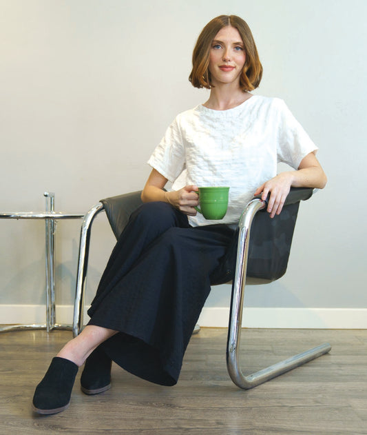 model in a white boxy pullover top with a light texture, worn with a wide leg navy blue pant