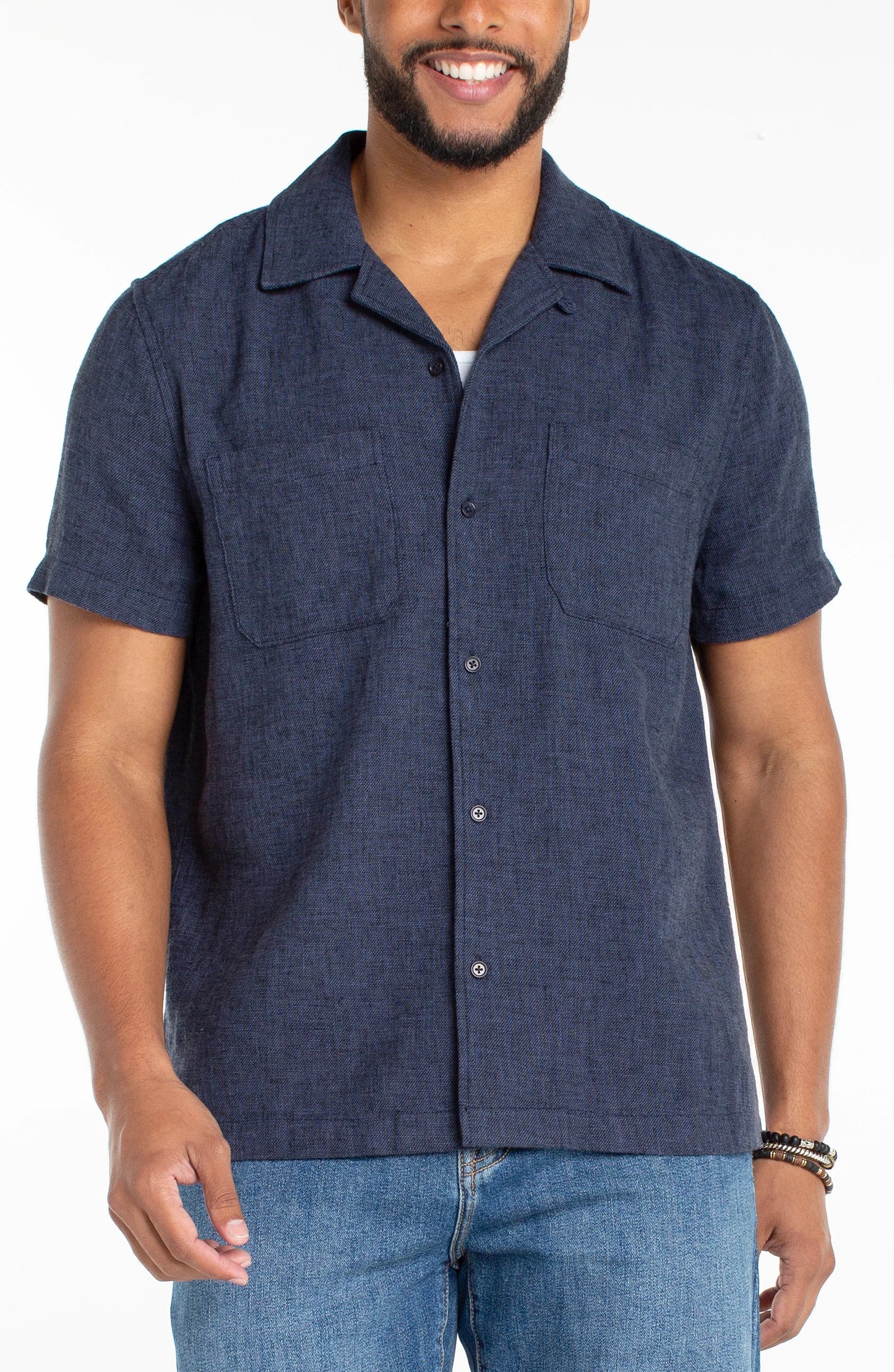 Man wearing a navy short-sleeve button-up shirt and jeans on a white background