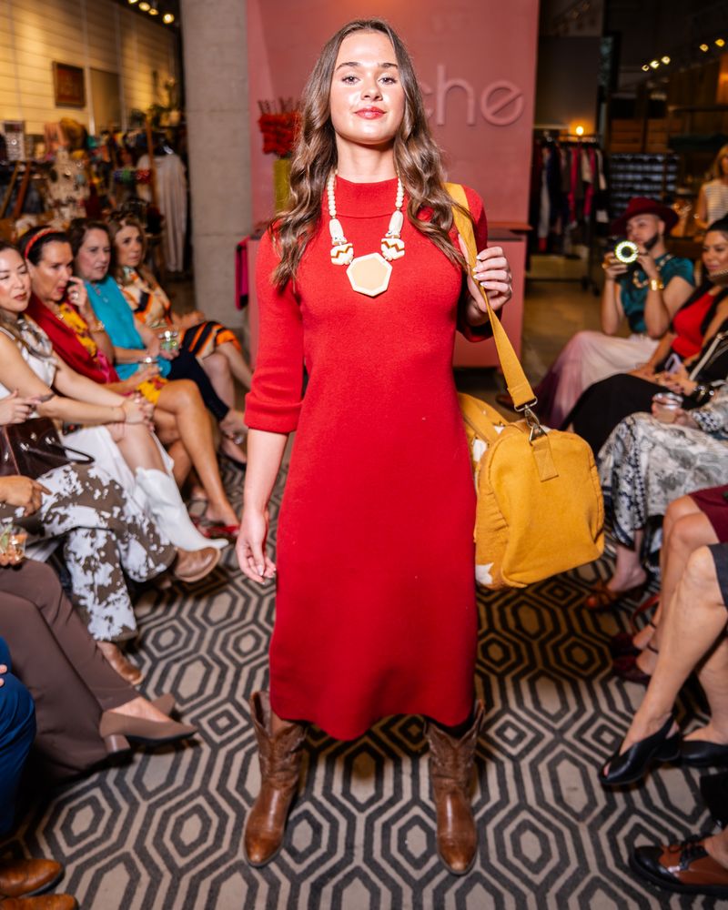 model wearing a red dress, chunky necklace and cowboy boots holding a yellow bag on a runway