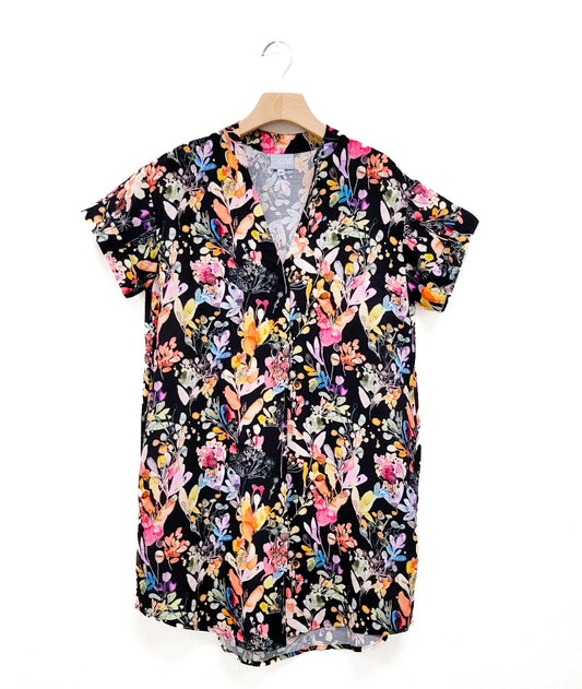 black boxy dress colorful flowers, short cuffed sleeves, v-neck and rounded hem on a hanger.