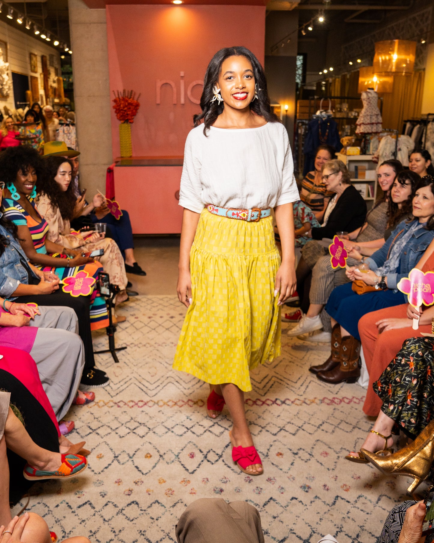 Woman in a white top and yellow skirt standing in front of an audience in a store setting.
