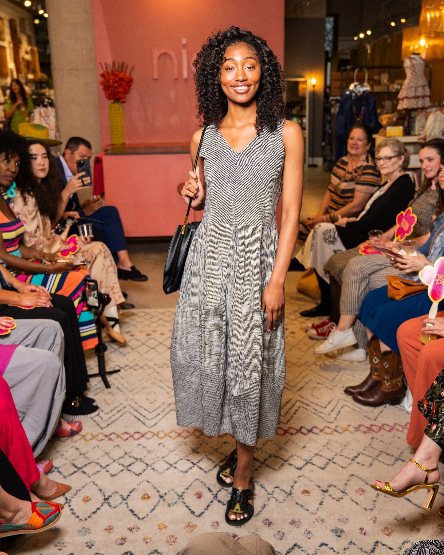 Woman in a black and white stripe dress and black purse walking down runway 
