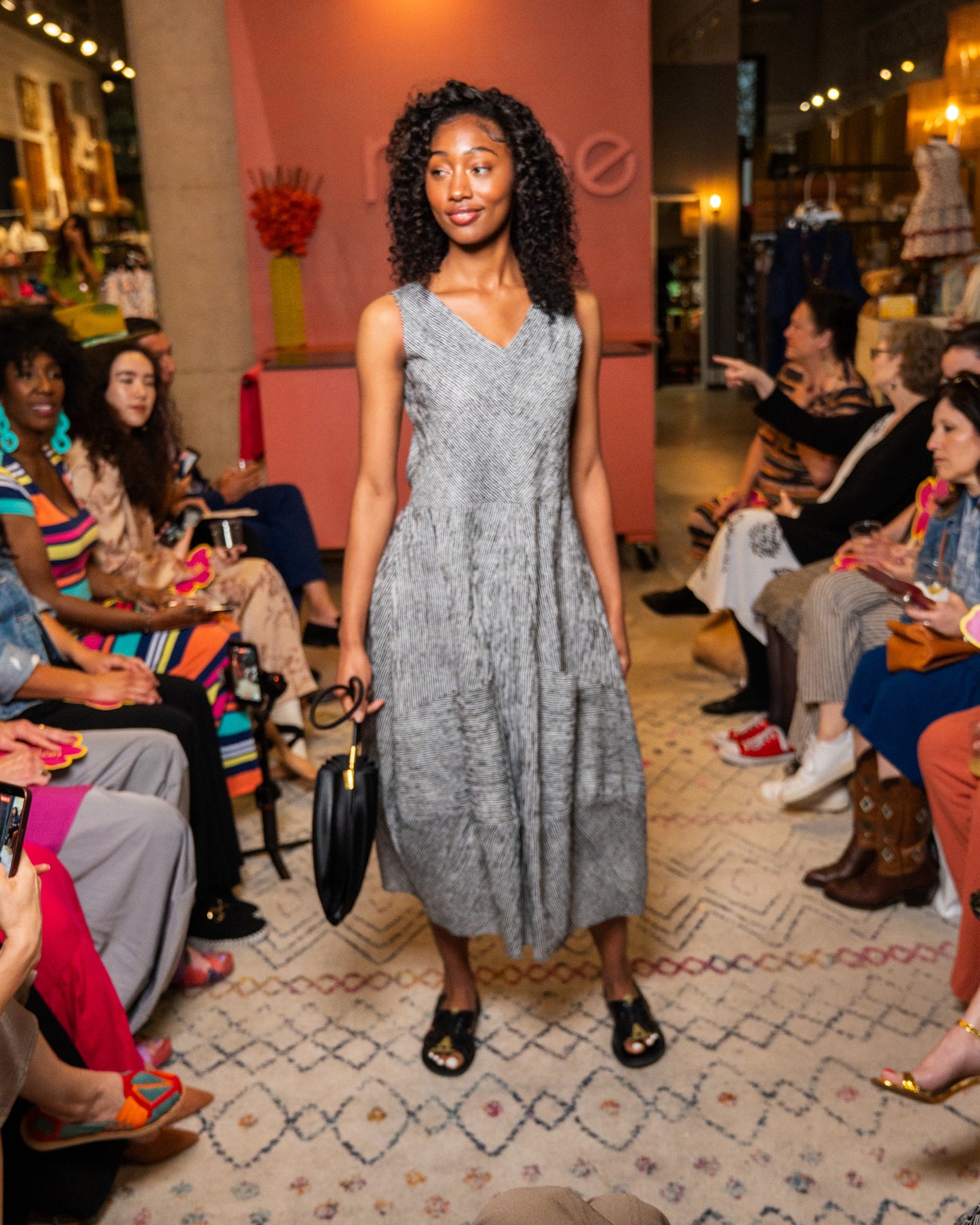 Woman in a black and white stripe dress and black purse walking down runway 