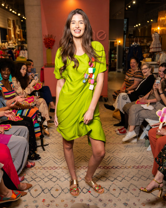 Woman in a bright green dress walking on a catwalk with an audience watching.