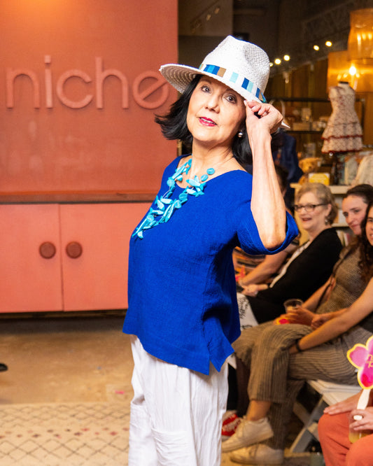 Woman in a blue top and white pants posing in a store with 'niche' branding.