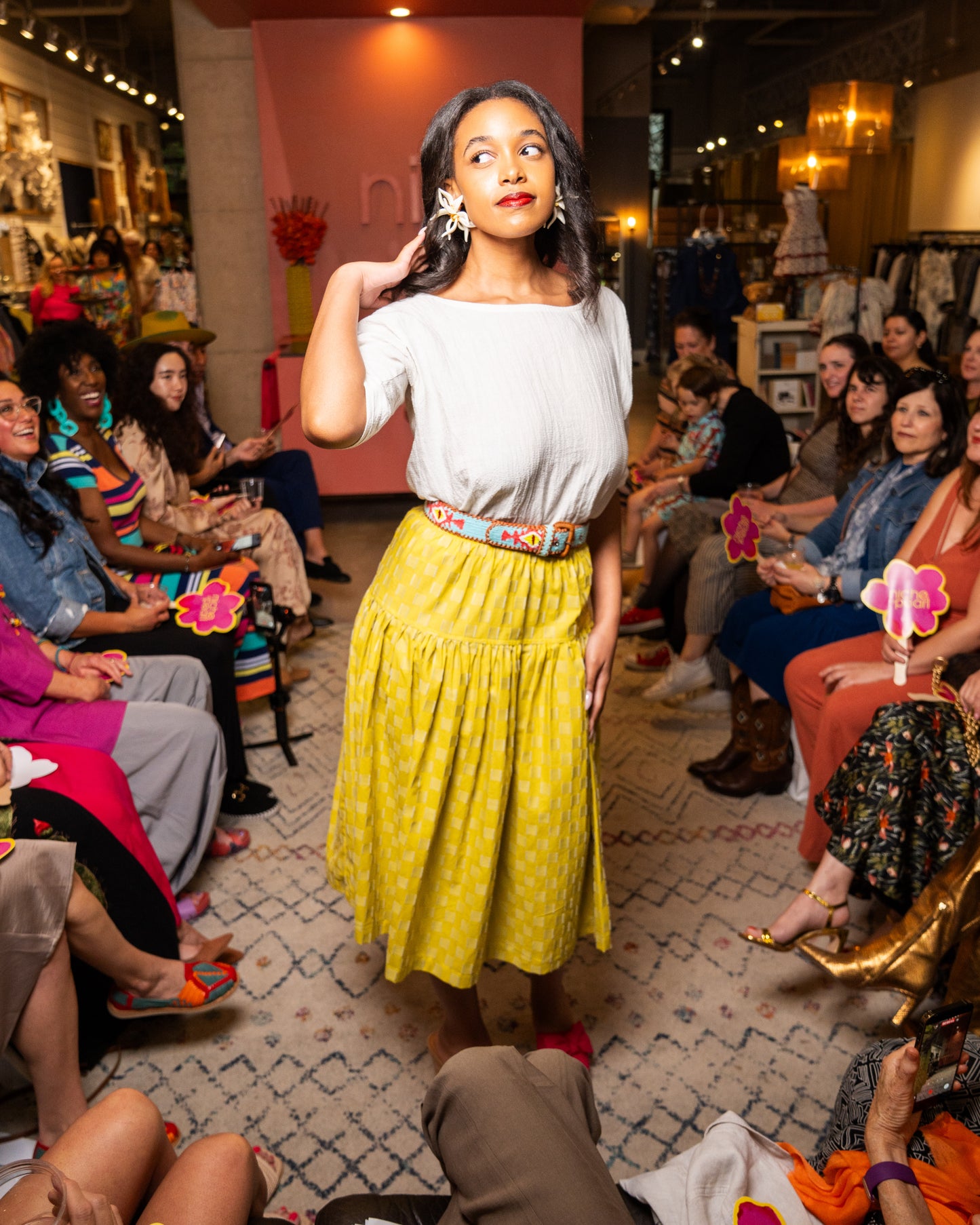 Woman in a yellow skirt and white top standing in front of an audience in a store setting.