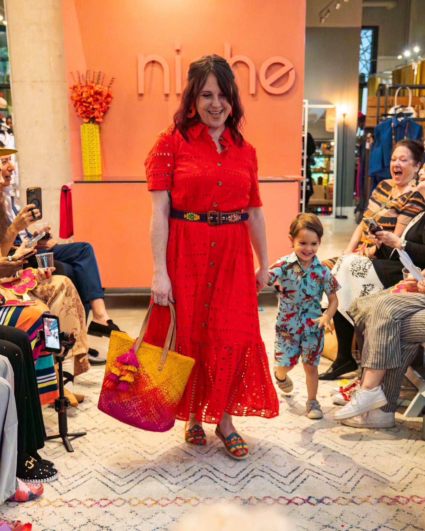 Woman in a red dress holding a colorful bag with a child on a runway