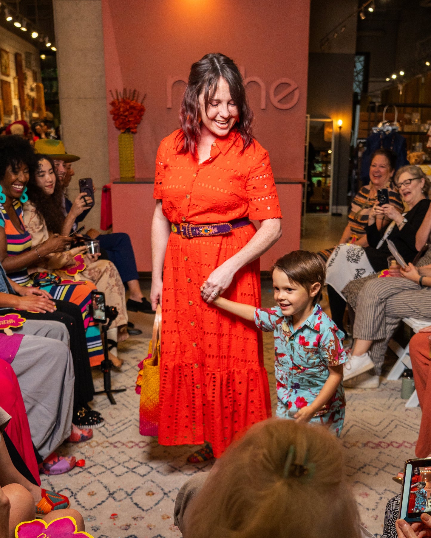 Woman in an red dress holding a child's hand on a runway