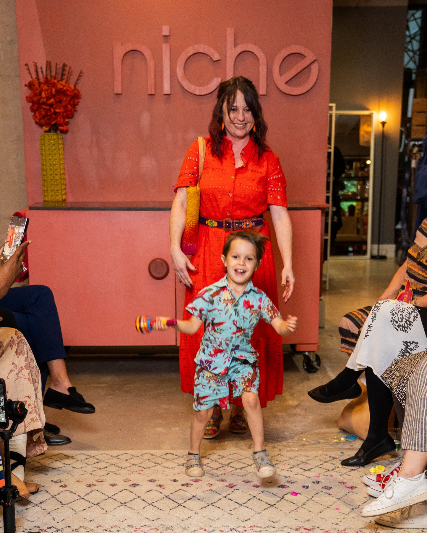 Woman in red dress with child in colorful outfit at 'niche' event
