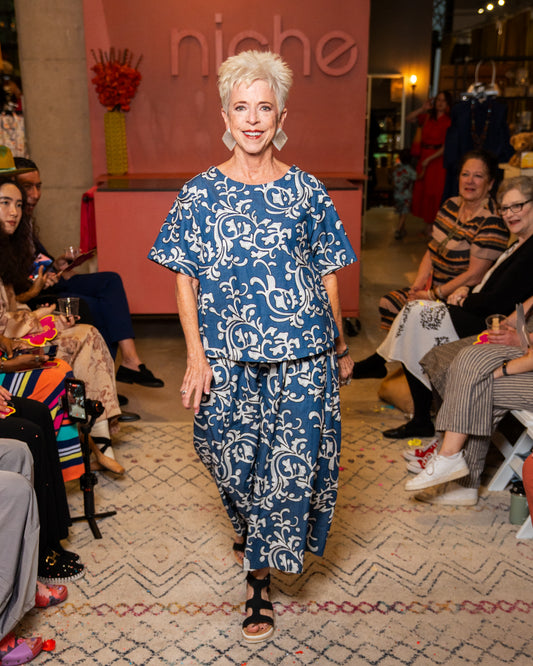 Woman in blue and white patterned outfit walking on a catwalk with 'niche' branding in the background.