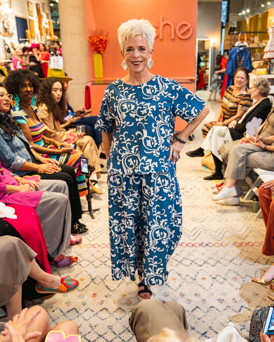 Woman in a blue floral dress walking on a catwalk with an audience watching.
