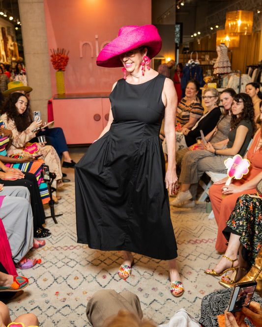 Woman in a black dress and pink hat at a fashion event with an audience.