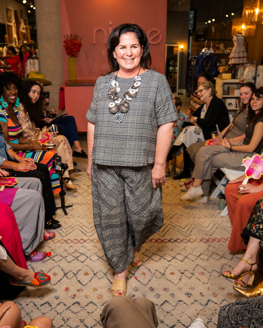 Woman in a checkered outfit standing in a room with people and decor.
