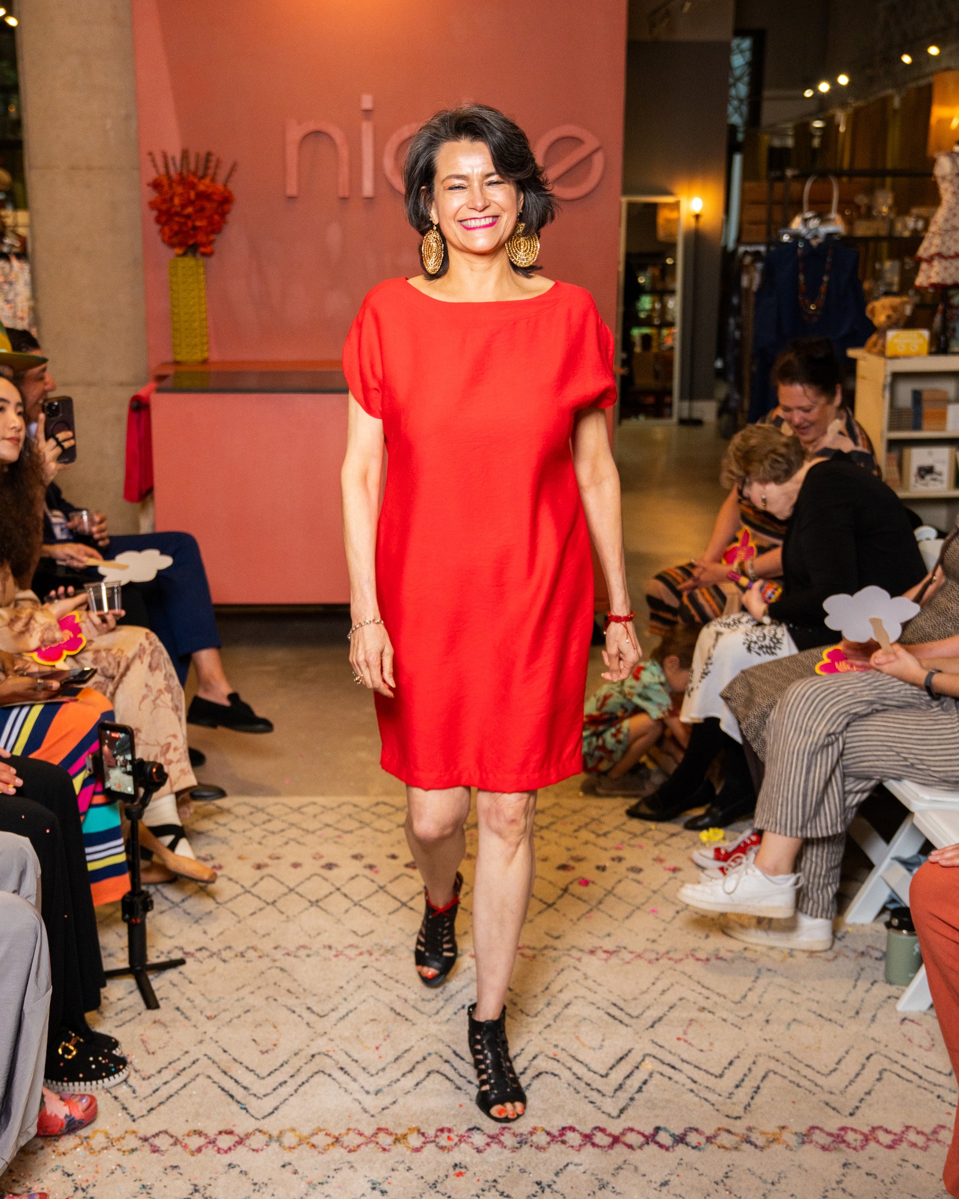 Woman in a red dress walking on a catwalk with 'nicole' branding in the background.
