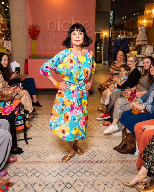 Woman in a colorful dress standing on a runway with an audience in a fashion show setting.
