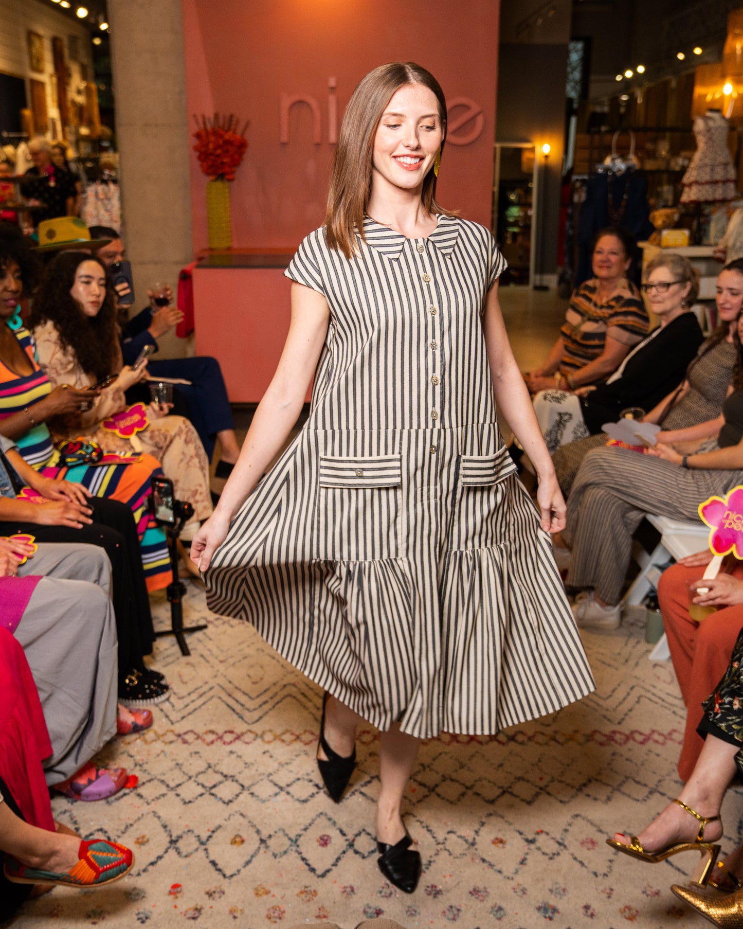 Woman in a black and white striped dress walking on a catwalk with an audience watching.