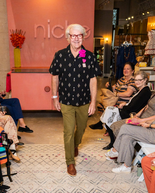 Man wearing a black patterned shirt and red glasses standing in a fashion show