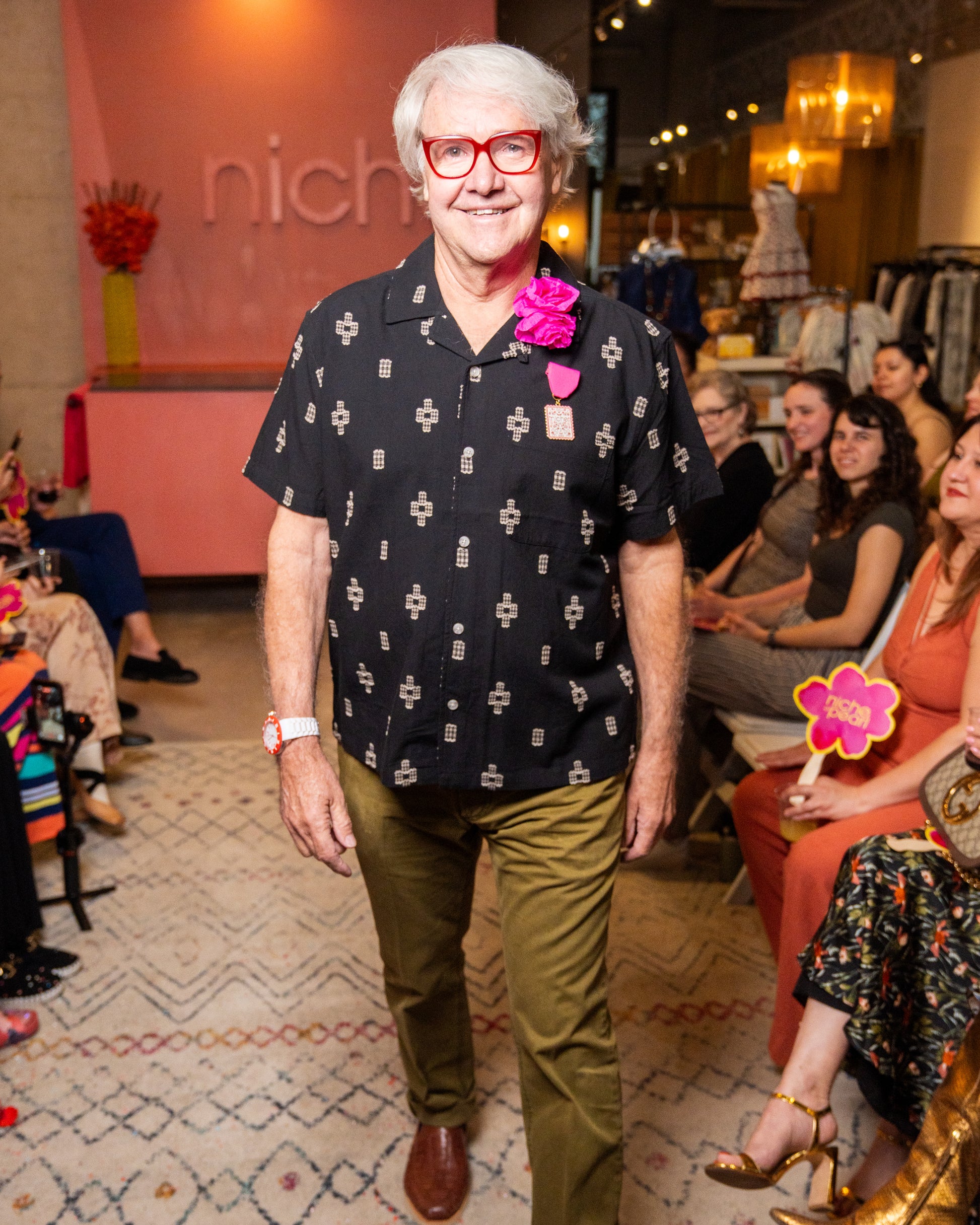 Man wearing a black patterned shirt and red glasses standing in a fashion show