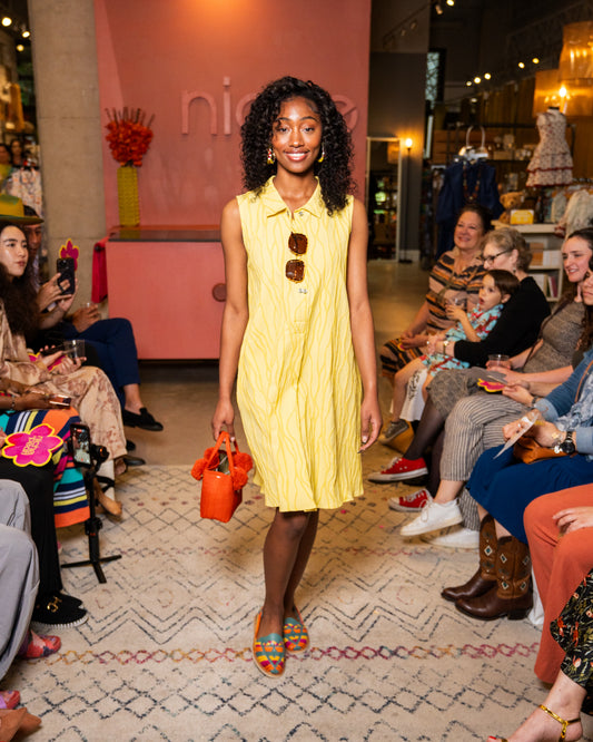 Woman in a yellow dress holding an orange handbag at a fashion event.