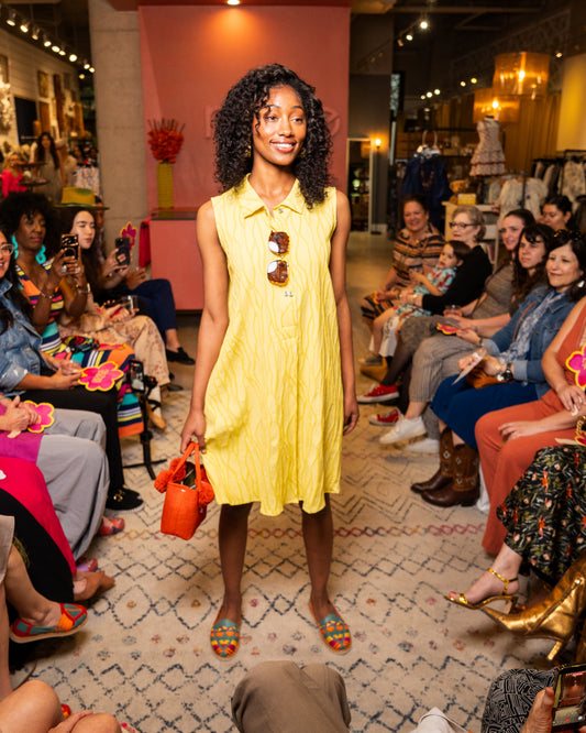 Woman in a yellow dress holding orange shoes at a fashion event.