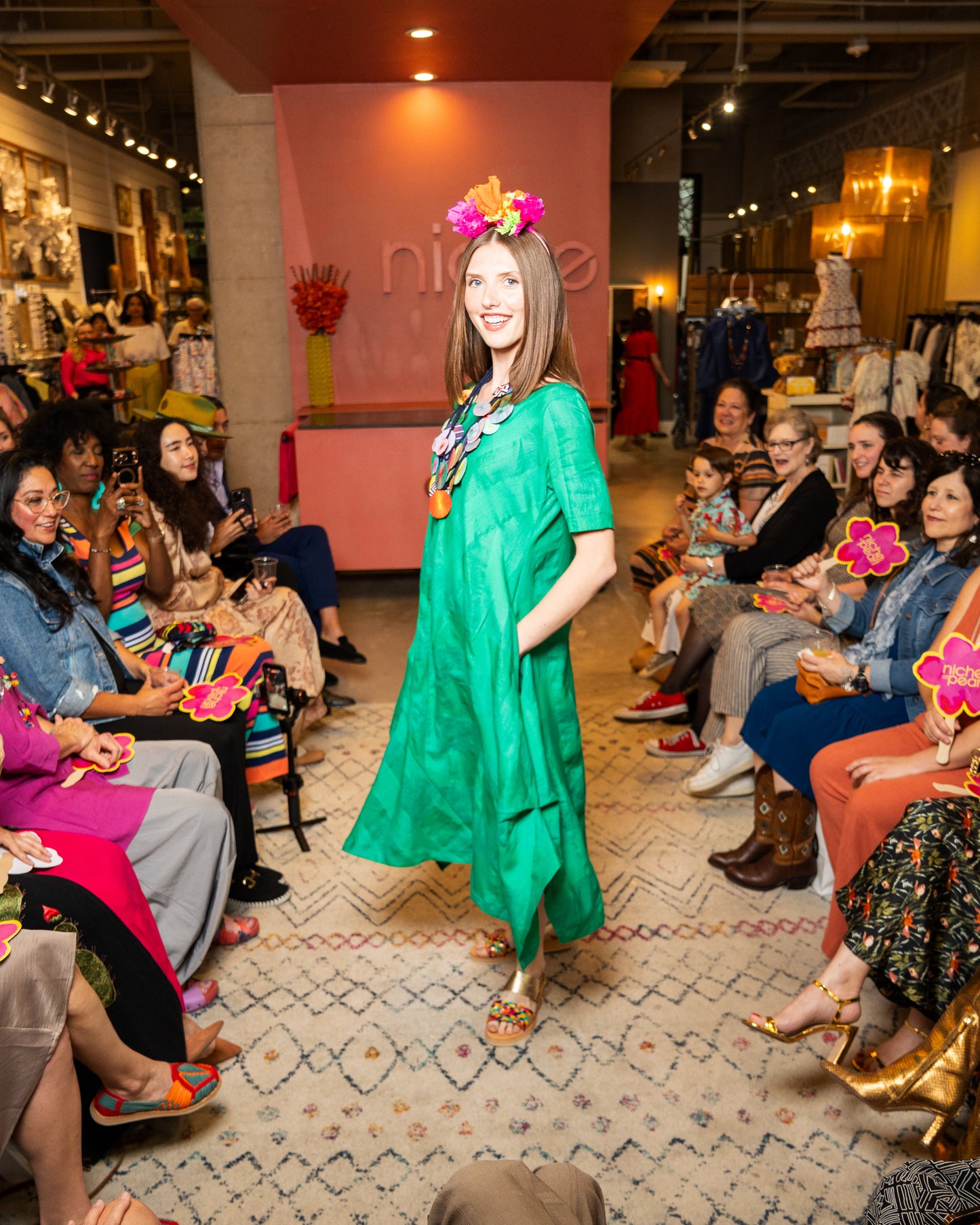 Woman in a green dress walking on a catwalk with an audience watching.