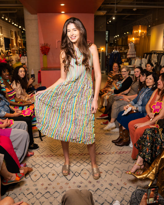 Woman in a colorful dress walking on a catwalk with an audience watching.