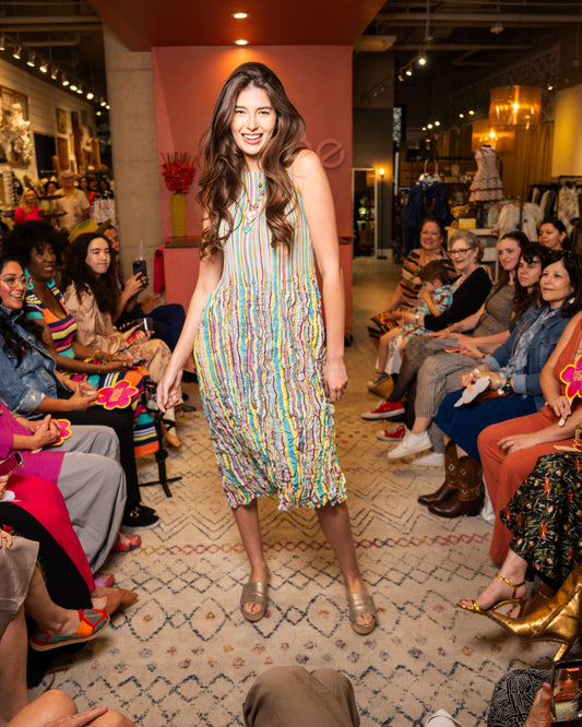 Woman in a colorful dress walking on a catwalk with an audience watching.