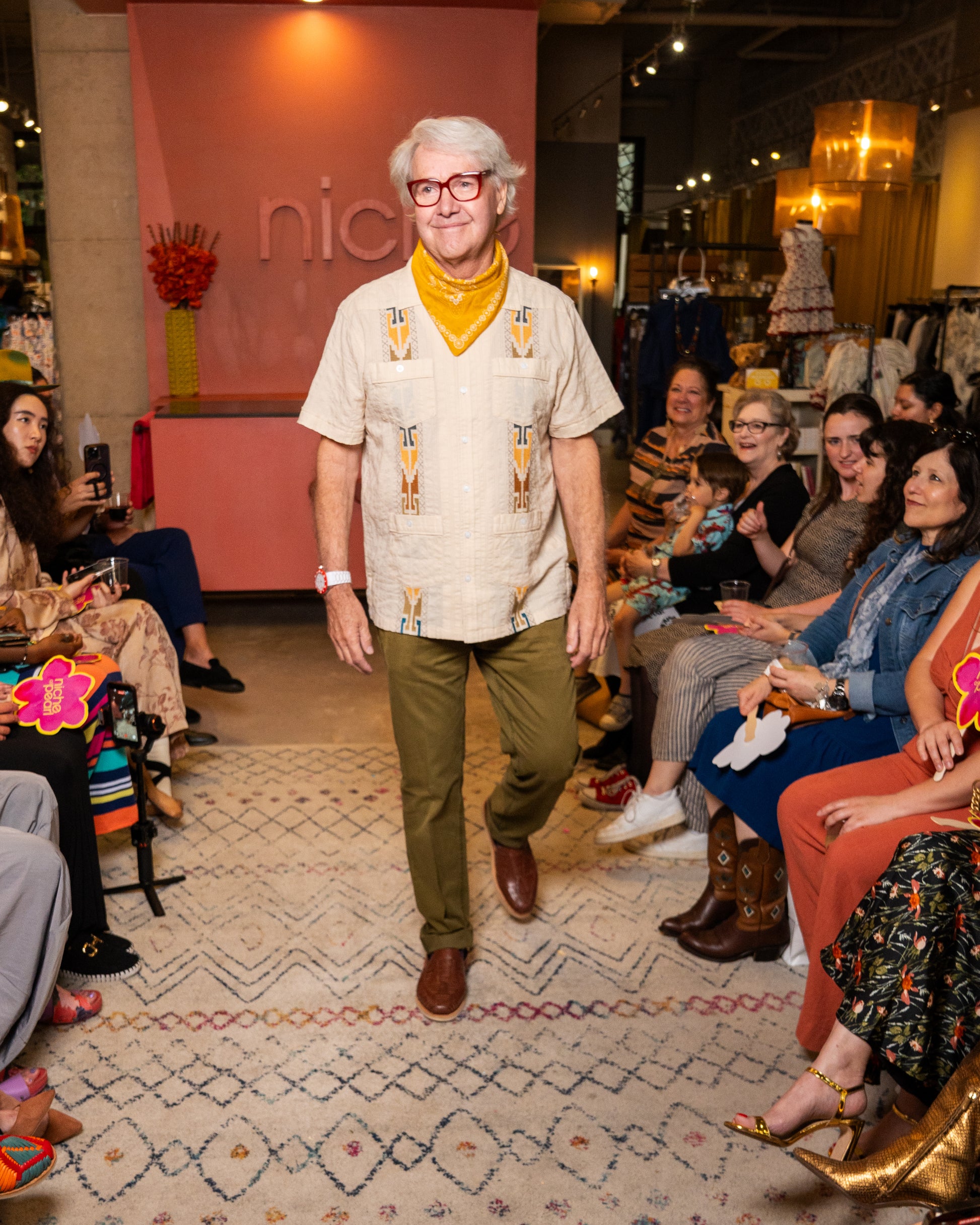 Man wearing guayabera and green pants while walking on a runway at a fashion event 