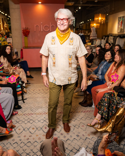 Man wearing guayabera and green pants while walking on a runway at a fashion event 

