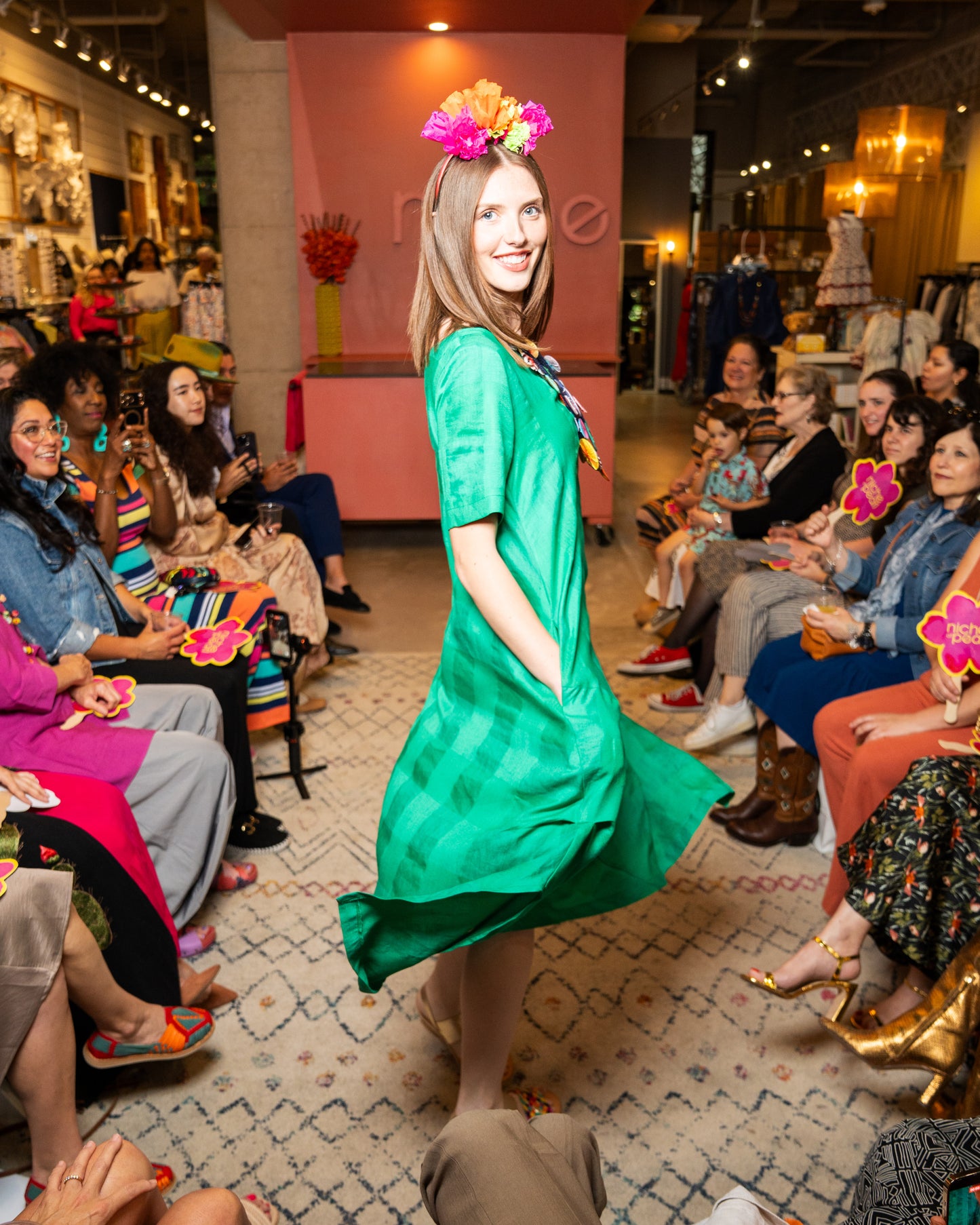 Model in a green dress walking on a catwalk with an audience watching.