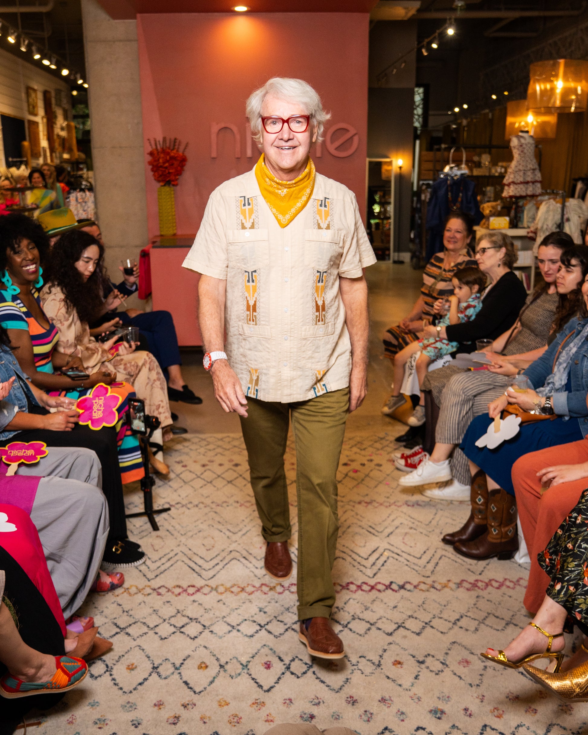Man wearing guayabera and green pants while walking on a runway at a fashion event 